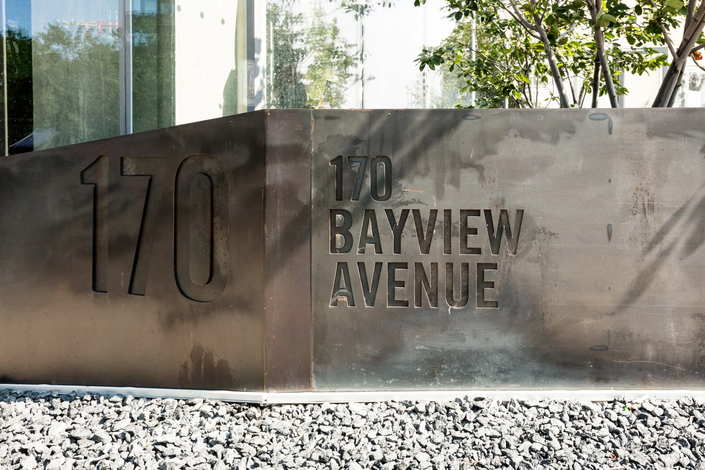 Custom metal address sign framed by black stone and greenery at 170 Bayview Avenue